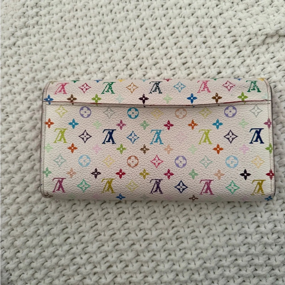 A Louis Vuitton monogram wallet in multicolor pastel and bright monogram canvas, placed on a textured off-white woven blanket.