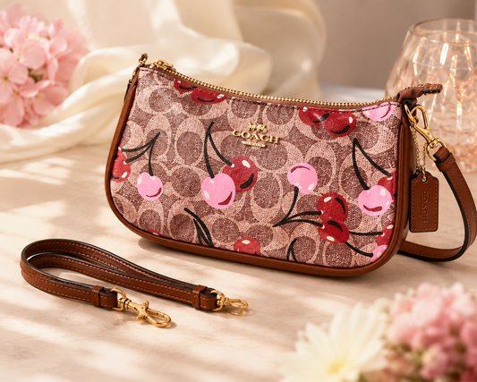 Coach cherry print wristlet crossbody bag with pink and brown signature-style canvas, brown trim, gold-tone hardware, and detachable strap